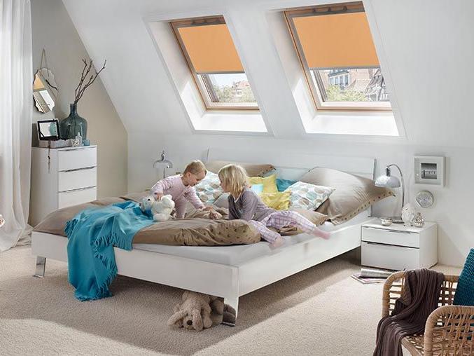Zwei Kinder spielen auf dem Bett im Schlaffzimmer, der Raum wird von Rollos an zwei Dachfenstern aus Holz zum Teil verdunkelt